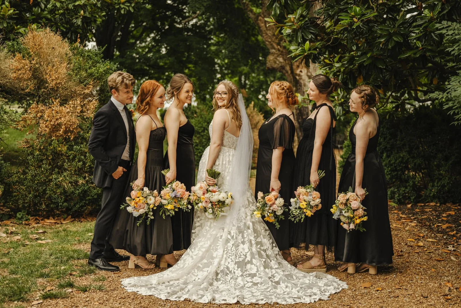 A bride with her bridesmaids in black dresses holding colorful bouquets